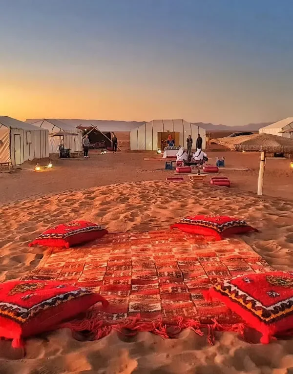 A serene desert scene featuring tents and colorful pillows arranged on the warm sand on our 2-Day Desert Tour from Marrakech to Zagora