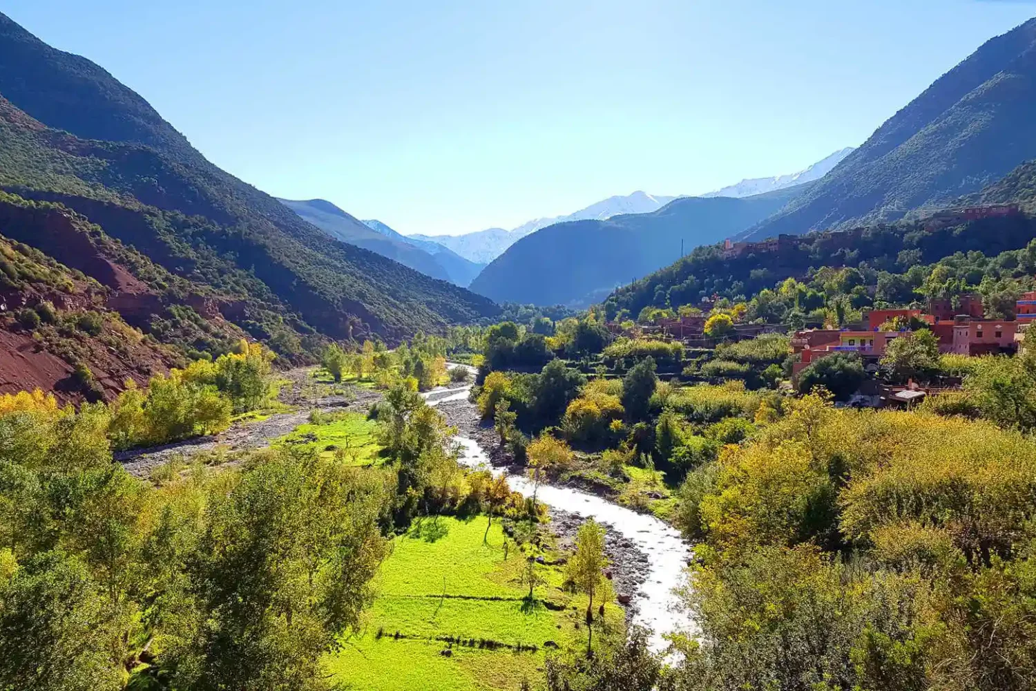 A serene river flows through a lush valley, framed by majestic mountains in the background.